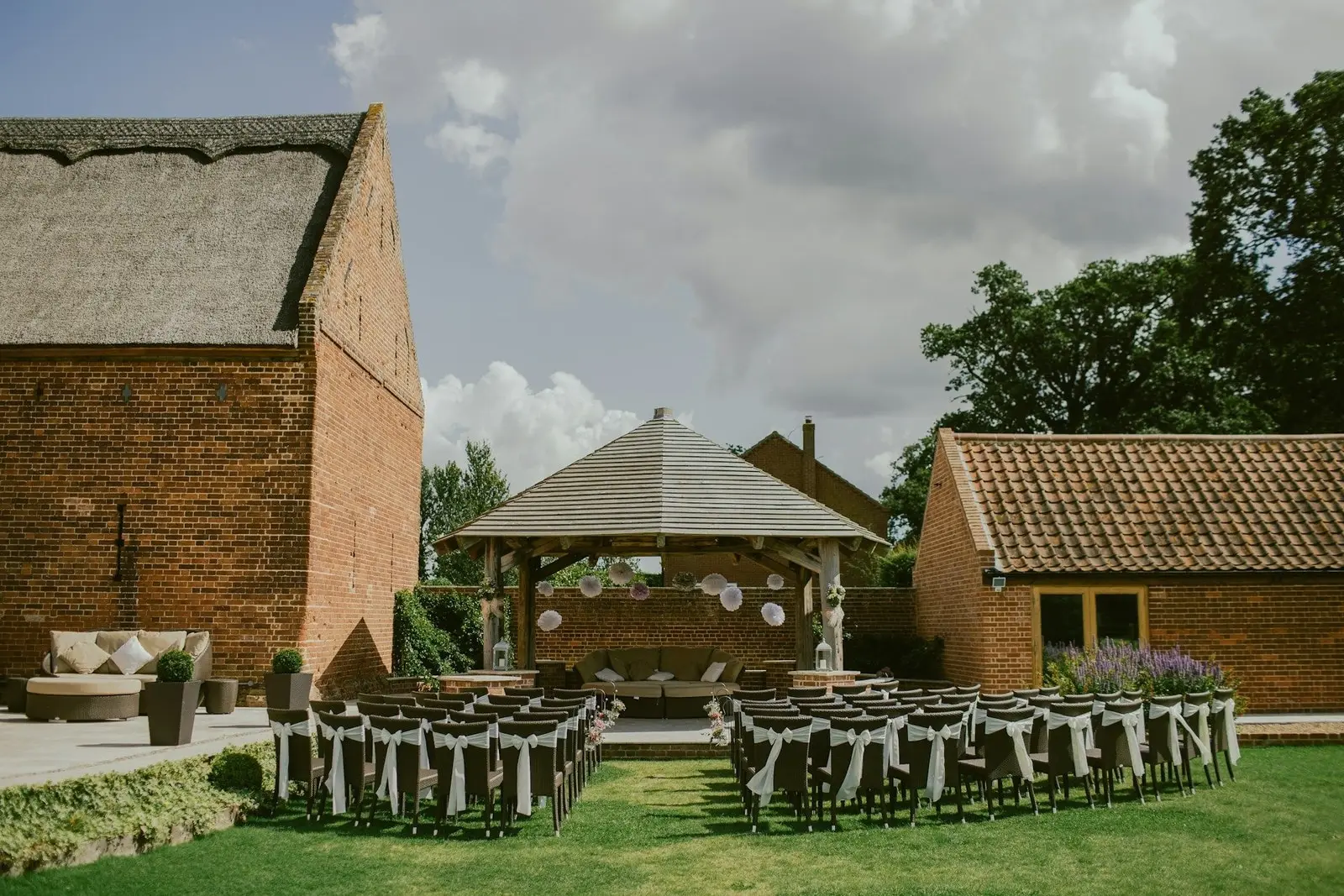 Jardín de la hacienda con sillas vestidas y una pérgola entre construcciones de ladrillo