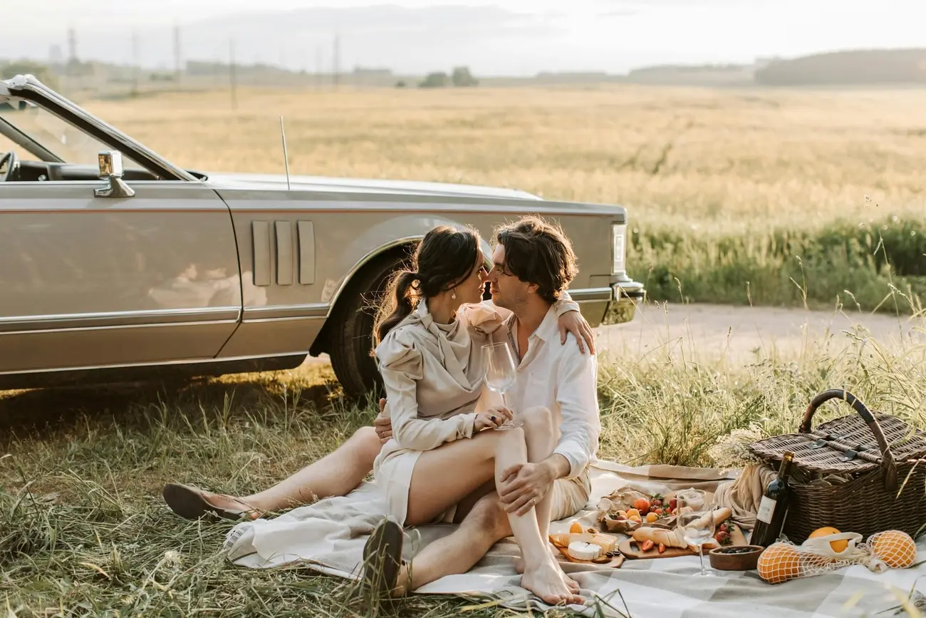 Irene y Emilio de picnic junto a un auto clásico, frente a un trigal