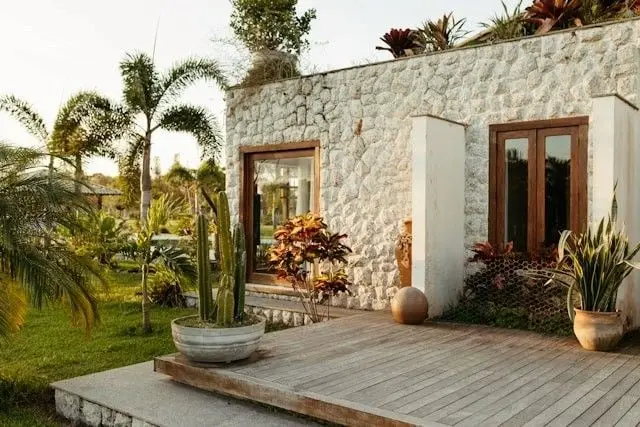 Casa de piedra blanca con terraza de madera y palmeras