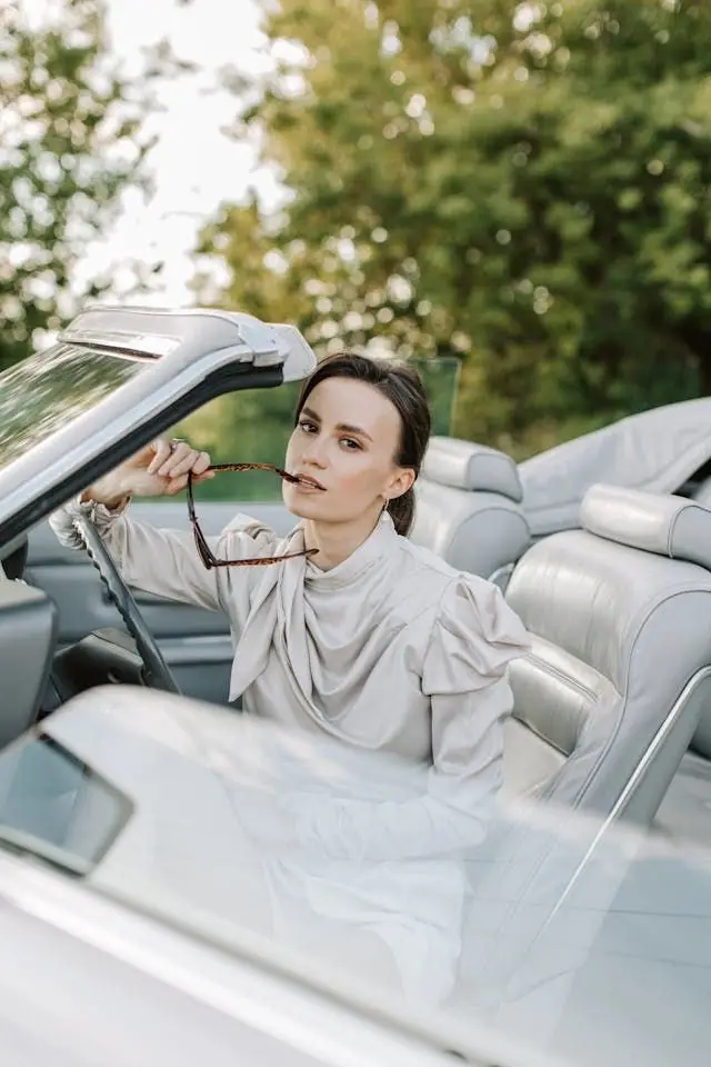 Retrato de Irene sentada en un auto convertible, con lentes en la mano