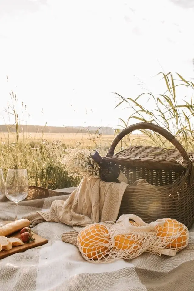 Canasta de picnic con naranjas y copas junto a un campo de trigo